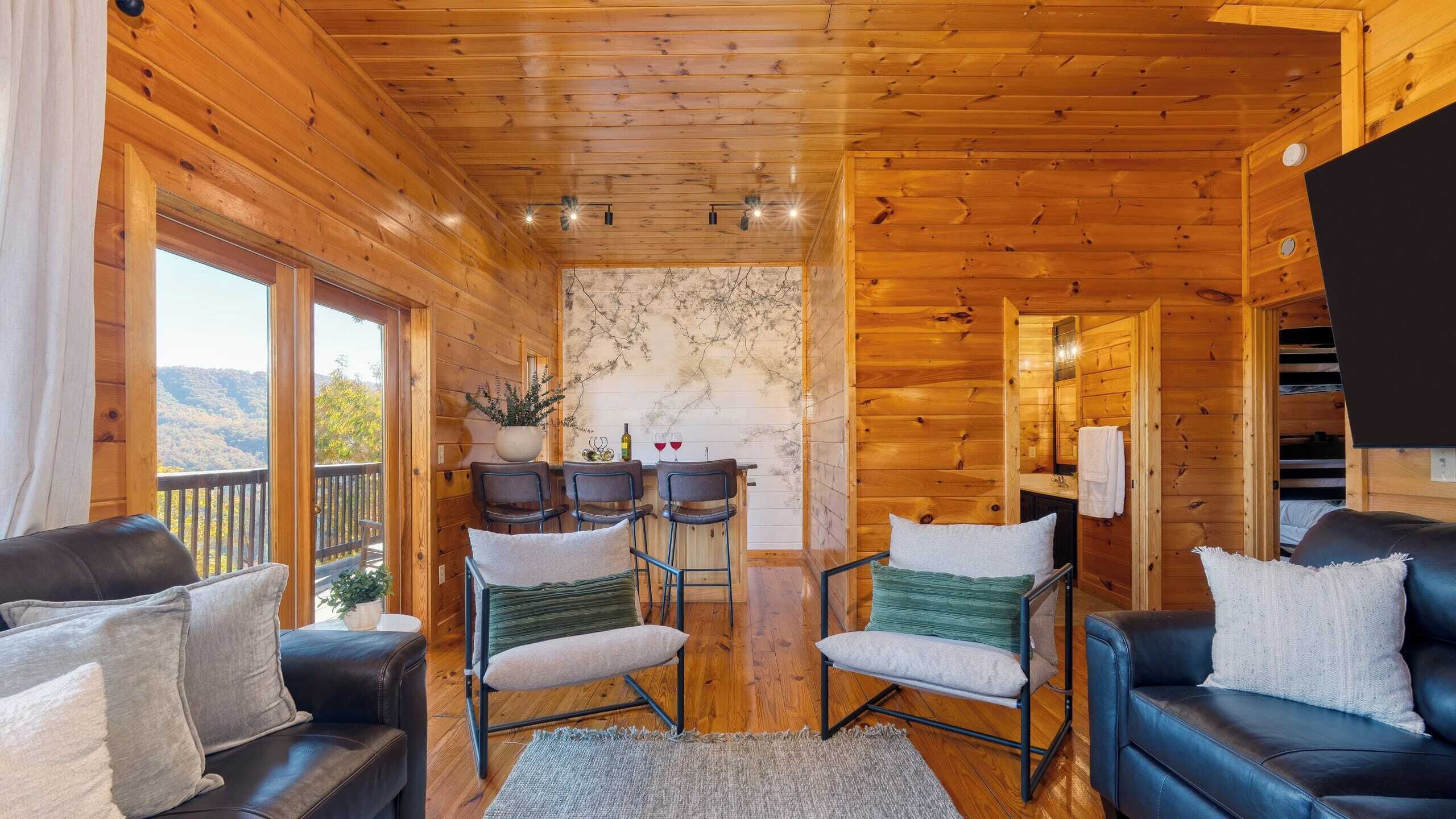 A wooden cabin interior with a dining area, two sofas, and a view of the outdoors.