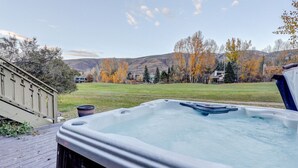 A hot tub in a backyard with a wooden deck, a grassy lawn, and autumn trees in the background. - EagleVail Getaway | Ski, Golf & Hot Tub (Avon)