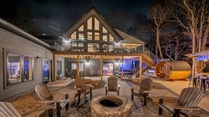 Uma casa grande com varanda coberta, poltronas Adirondack e lareira de pedra.