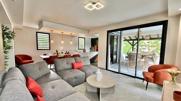 Een moderne woonkamer met een grijze modulaire bank, een ronde salontafel en een eethoek met een tafel en stoelen.