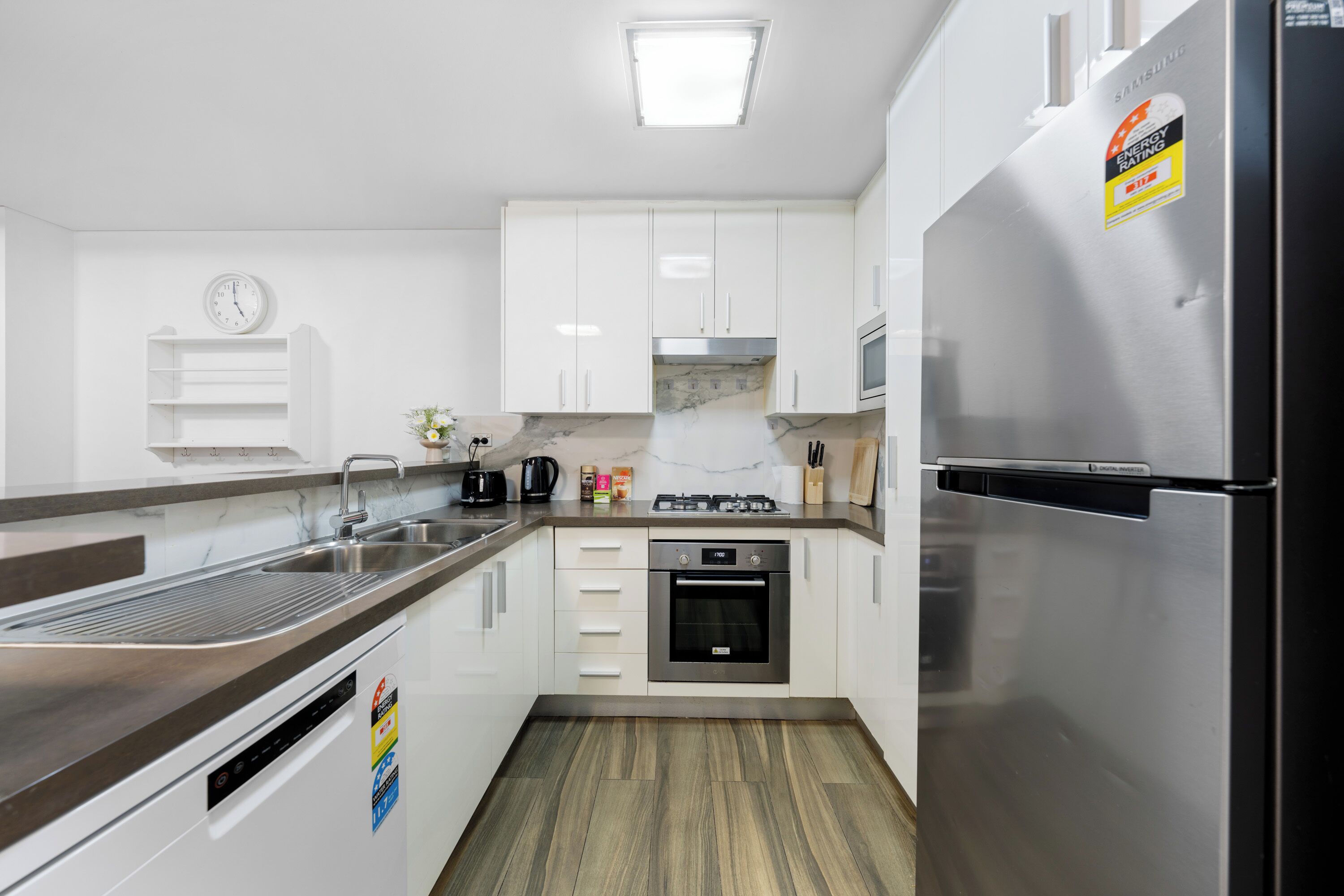 A modern kitchen with white cabinets, stainless steel appliances, a built-in oven, and a microwave.