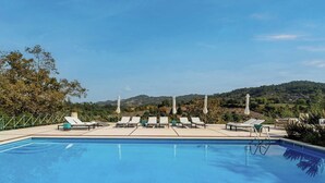 Piscina com espreguiçadeiras e vista para colinas.