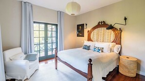 Quarto com uma cama grande, uma cadeira, um abajur e uma janela com cortinas.