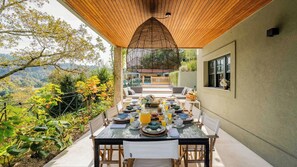 Un espacio exterior para comer con una mesa dispuesta para el desayuno, rodeado de follaje y con vistas a un paisaje pintoresco.