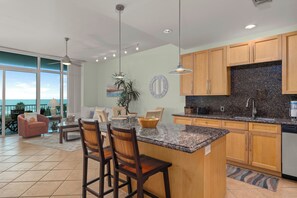 A modern kitchen with a granite countertop, wooden cabinets, and a large island with bar stools. - Sapphire #503 | Luxury Beachfront Condo • Gulf Views • Resort Amenities (South Padre Island)