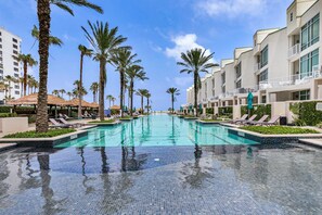 Ein Schwimmbecken mit Liegestühlen und Palmen, umgeben von Hotelgebäuden.