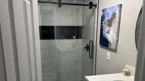 A modern bathroom with a glass-enclosed shower, a toilet, and a sink with a marble countertop. - 60th Street Staycation (Lawton)