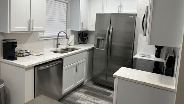 A modern kitchen with white cabinets, stainless steel appliances, and a dishwasher. - 60th Street Staycation (Lawton)