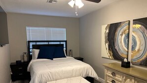 A bedroom with a bed, bedside tables, a dresser, a ceiling fan, and a window with blinds. - 60th Street Staycation (Lawton)