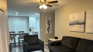 A living room with a dark-colored sofa, a wooden coffee table, and a ceiling fan. - 60th Street Staycation (Lawton)