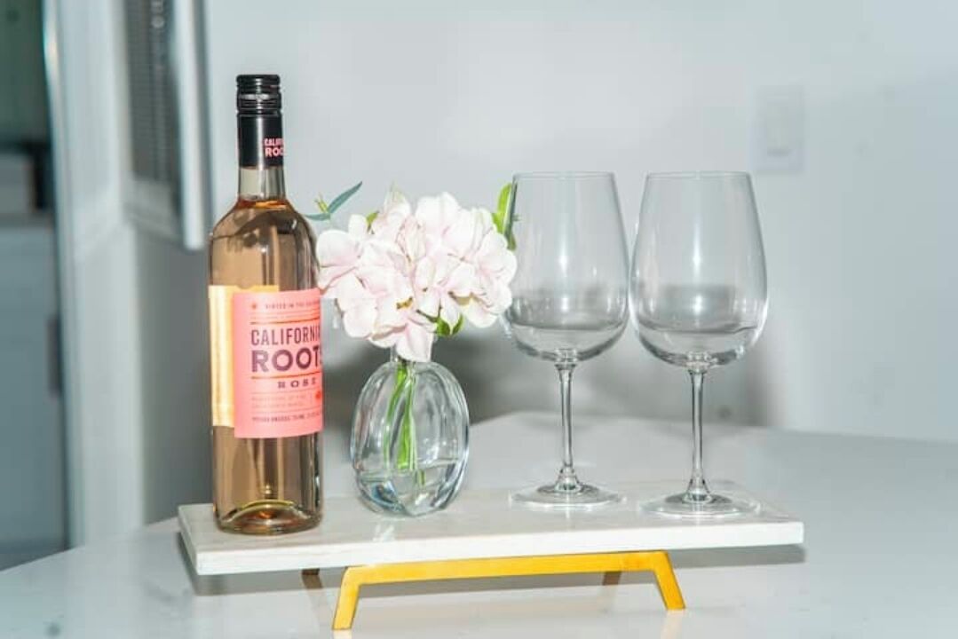 A bottle of California Root wine, a vase with flowers, and two wine glasses on a white table with a yellow base.