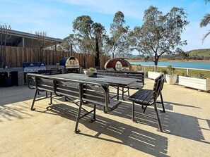 Un patio exterior con una parrilla, una mesa de madera y un área de estar con vista a un lago.
