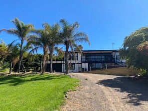 Un edificio moderno con camino de grava, palmeras y un cielo azul despejado.