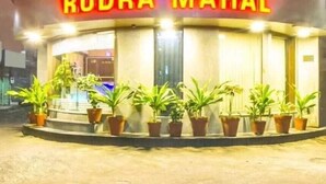 Un hotel llamado "Rudra Mahal" con un llamativo letrero de neón, plantas en macetas al frente y una entrada visible.