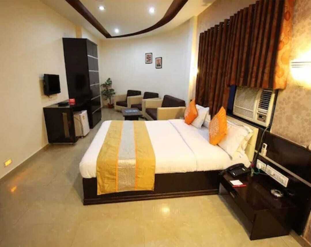 A hotel room with a large bed, a desk, a chair, a TV, and a wall-mounted heater.