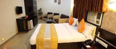 Quarto de hotel com cama grande, escrivaninha, cadeira, televisão e aquecedor fixado na parede.