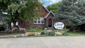 A rustic brick building with a sign reading "The Cottage Bed & Breakfast Inn" and a phone number. There are decorative sheep statues and a sign that says "THE COTTAGE".