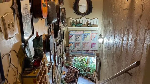 Eine Treppe führt zu einem Raum mit einer gepolsterten Wanddecke, einem alten Coca-Cola-Kühlschrank und einem kleinen Tisch mit einer Pflanze.