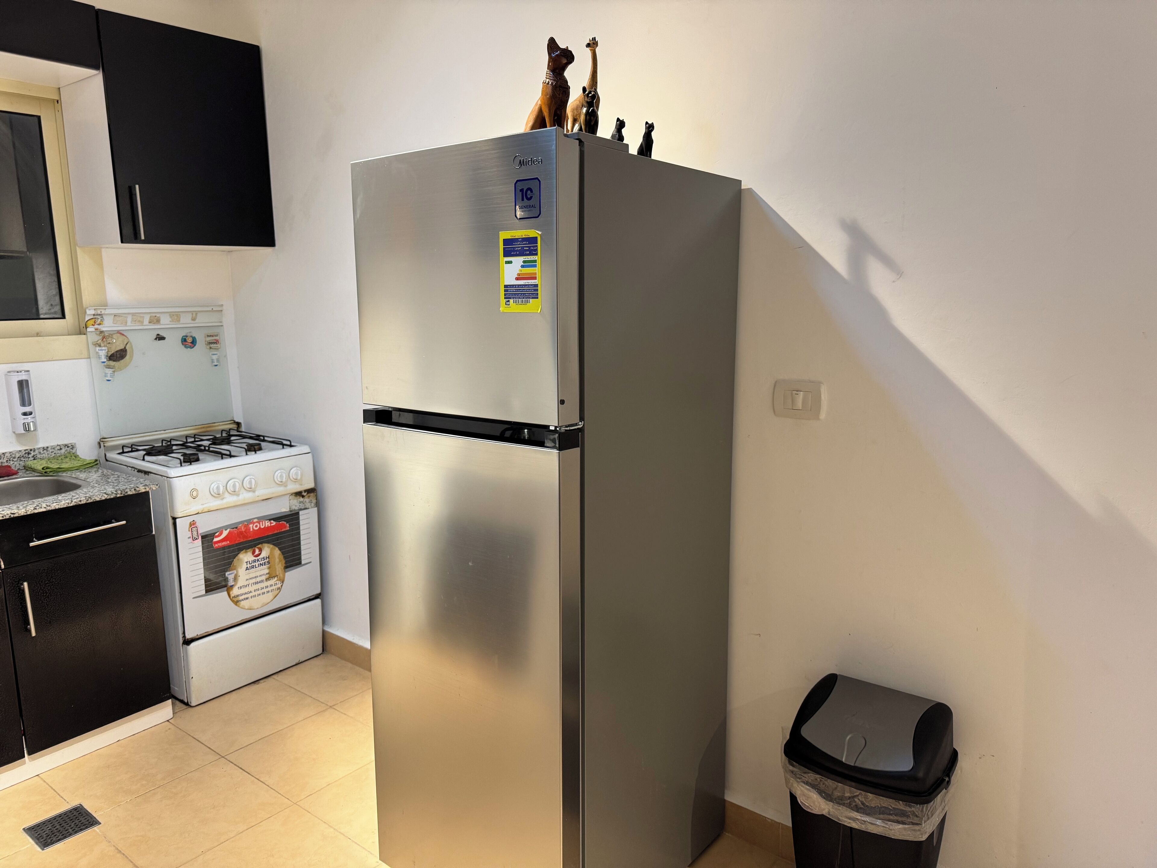 A kitchen with a stainless steel refrigerator, a gas stove, and a trash bin.
