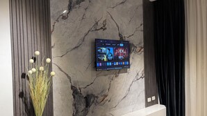 Un salon moderne avec un mur en marbre, un téléviseur fixé au mur, un vase contenant des plantes séchées et un rideau noir.