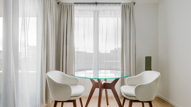 A modern dining area with a glass table and two chairs, large windows with sheer curtains, and a city view. - Blueground | Chalk Farm, balcony, nr Primrose Hill (London)