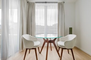 A modern dining area with a glass table and two chairs, large windows with sheer curtains, and a city view. - Blueground | Chalk Farm, balcony, nr Primrose Hill (London)