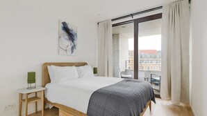 A modern bedroom with a wooden bed, white bedding, a green bedside lamp, and a city view through large windows. - Blueground | Chalk Farm, balcony, nr Primrose Hill (London)
