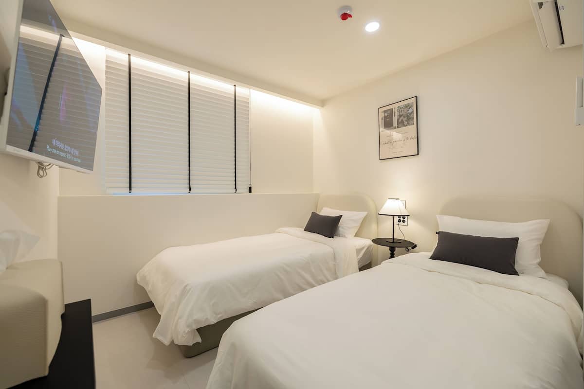 Een hotelkamer met twee eenpersoonsbedden, een aan de muur bevestigde televisie, een nachtkastje met een lamp en een lijst met een afbeelding aan de muur.
