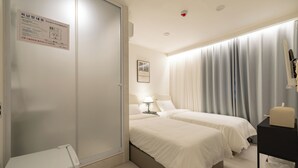 Hotelkamer met twee bedden, een nachtkastje met lamp, een kledingkast en een raam met gordijnen.