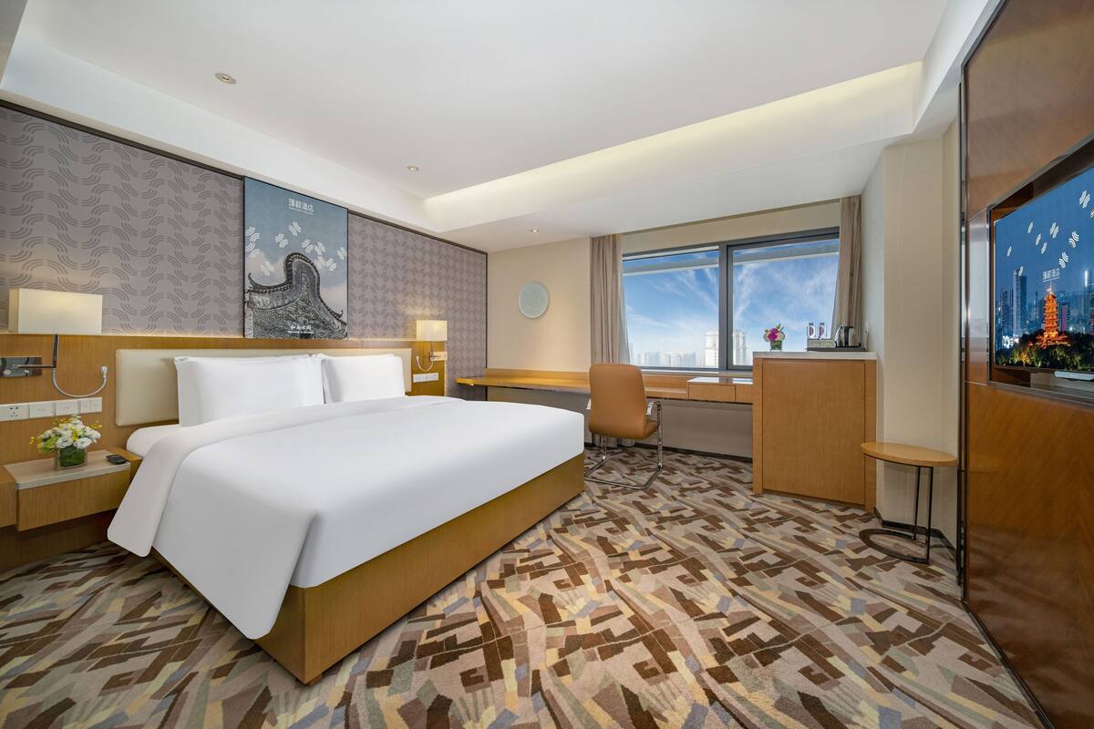 Habitación de hotel con una cama grande, un escritorio, una silla y vistas a la ciudad.