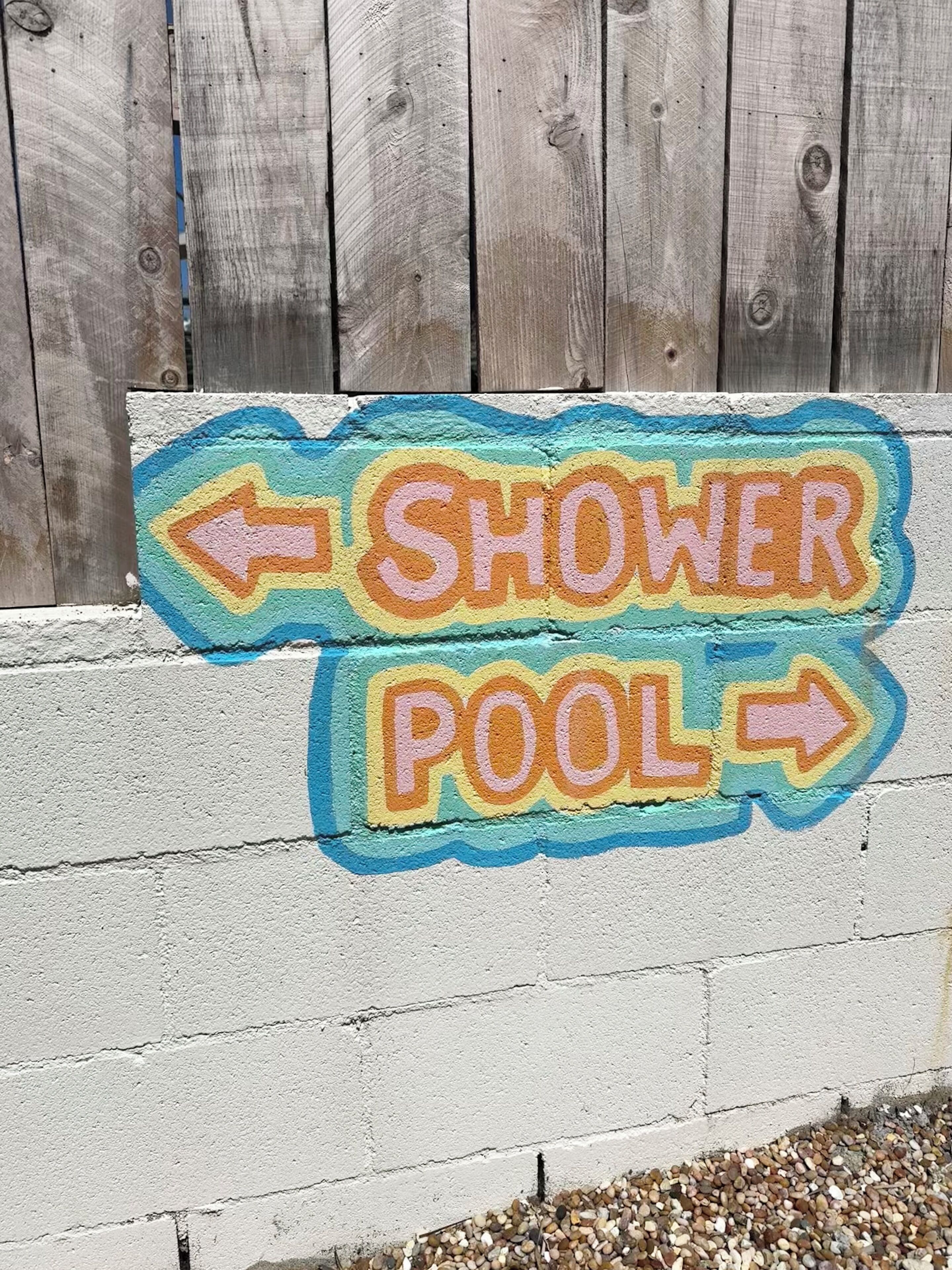 En färgglad skylt på en vägg som visar var en duschplats med tillhörande pool finns, och den har pilar som anger riktningen.
