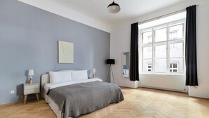 Et soveværelse med seng, sengeborde, gulvlampe, et vindue med gardiner og en radiator.