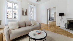 En rummelig stue med en beige sofa, et rundt sofabord og en pejs.