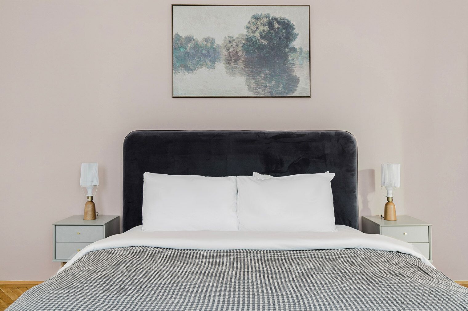 Camera da letto con una testiera imbottita nera, cuscini bianchi, coprip letto a quadretti e due comodini con lampade.