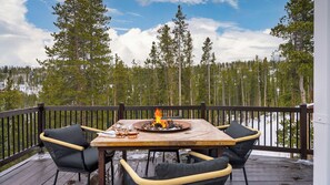 Eine Terrasse mit Tisch und Stühlen, einer Feuerstelle und Blick auf einen Wald und See.