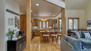 A spacious kitchen with wooden cabinets, a dining area with a gray sofa, and a kitchen island with bar stools. - Skate Bowl, Climbing Wall, Arcade Breckenridge Adventure Chalet by Avantstay (Breckenridge)