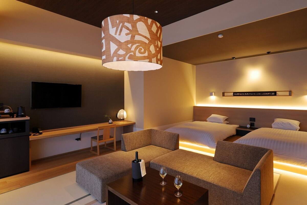 A hotel room with a bed, bedside tables, a TV, a desk, and a sofa.