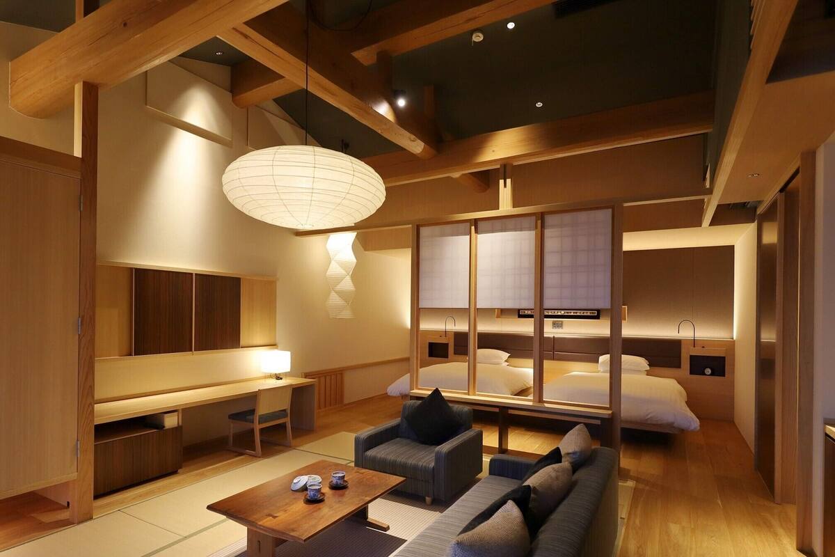 A modern hotel room with a wooden ceiling, a large bed, a desk, and a sofa.