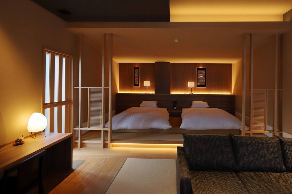 A hotel room with a bed, bedside tables, a sofa, and a view of the outside.