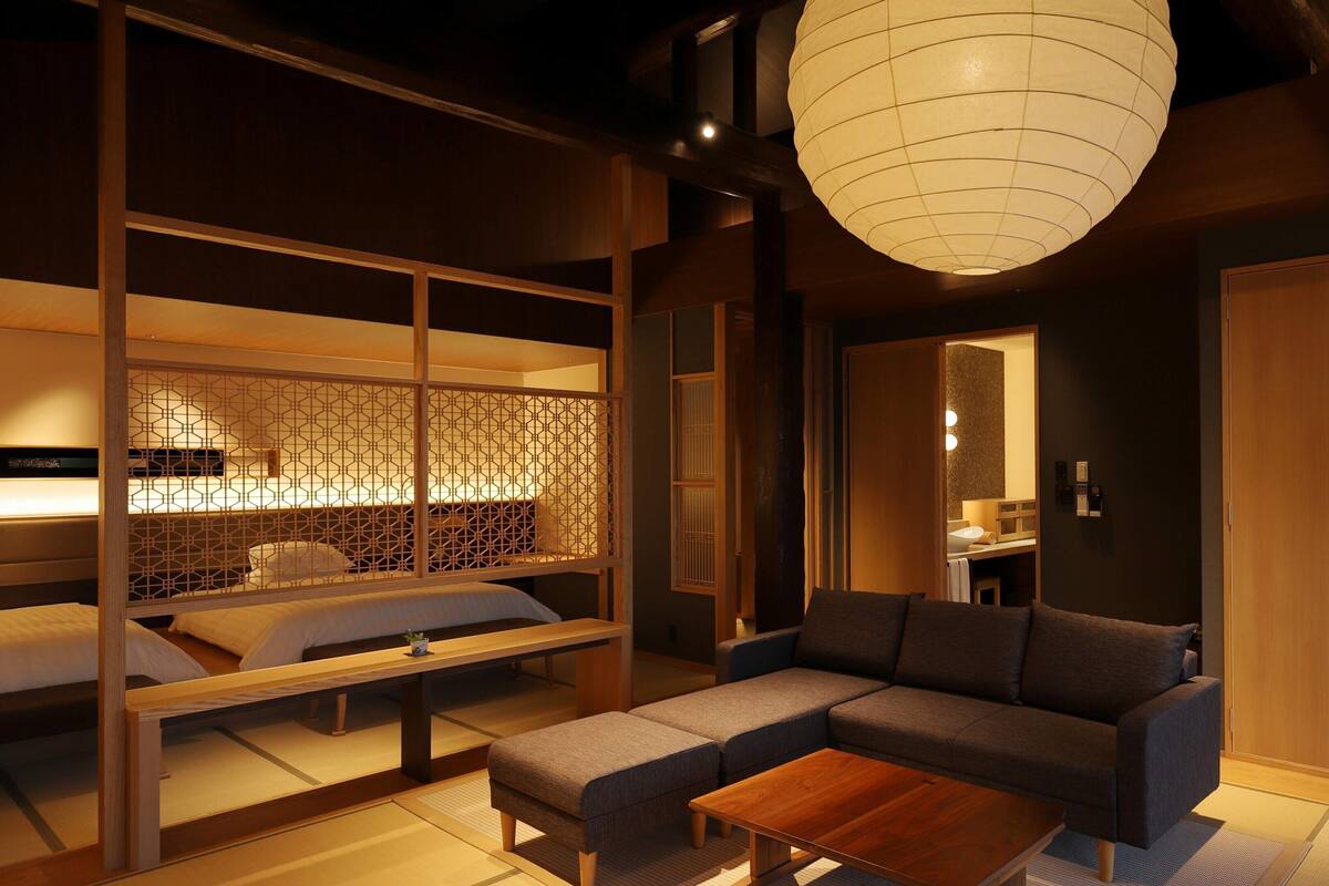 A traditional Japanese-style room with tatami flooring, a low wooden bed, a sofa, and a large hanging paper lantern.