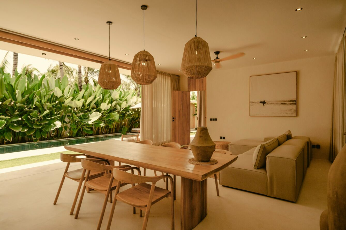 A modern dining area with a wooden table and chairs, a large vase, and hanging wicker lamps.