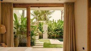 Une chambre dotée d’un grand lit, donnant sur un jardin tropical, et possédant une porte-fenêtre coulissante qui mène à l’extérieur.