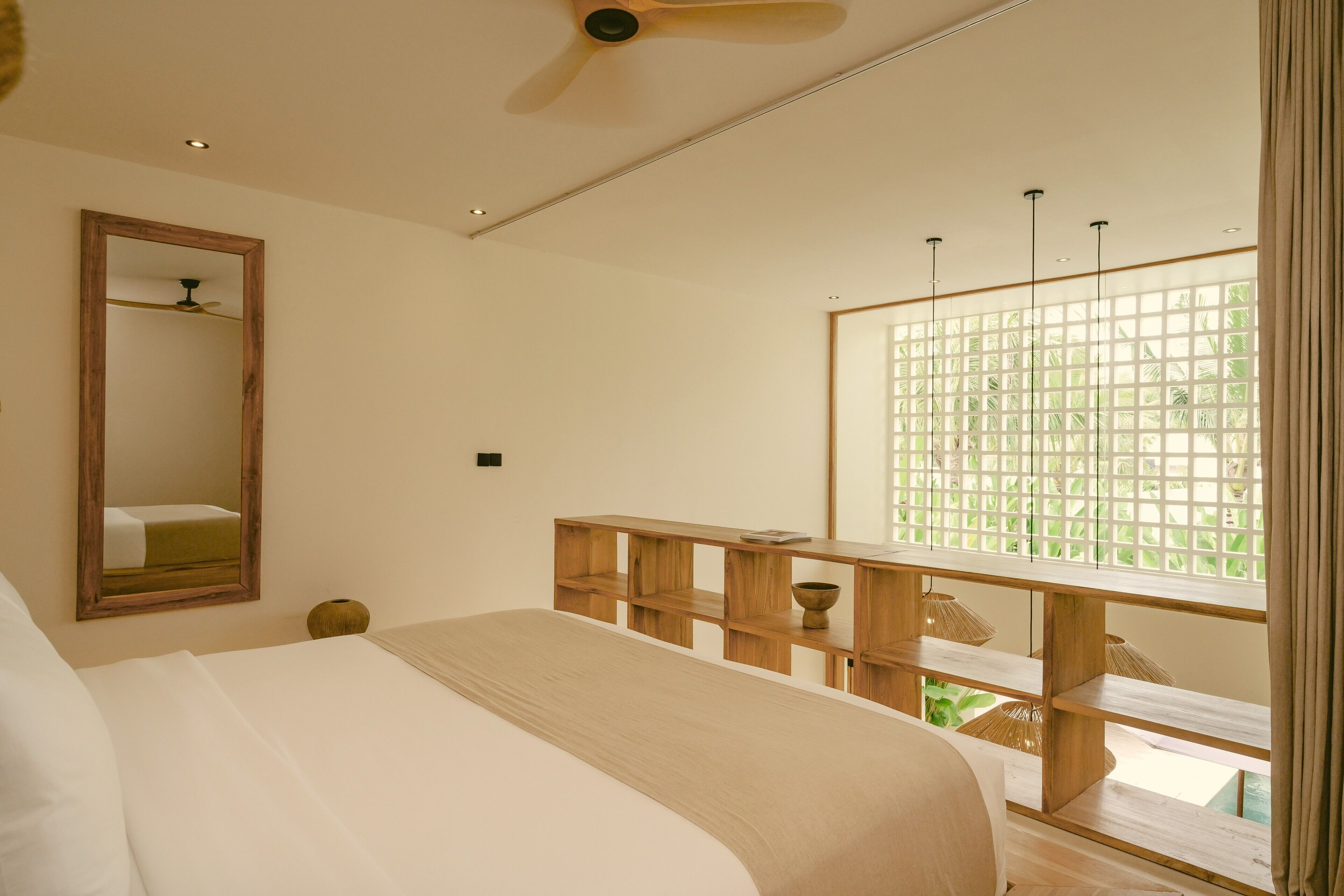 Ein Schlafzimmer mit Bett, einem Holfnachtkästchen, einem Spiegel und einem Fenster mit Blick ins Grüne.