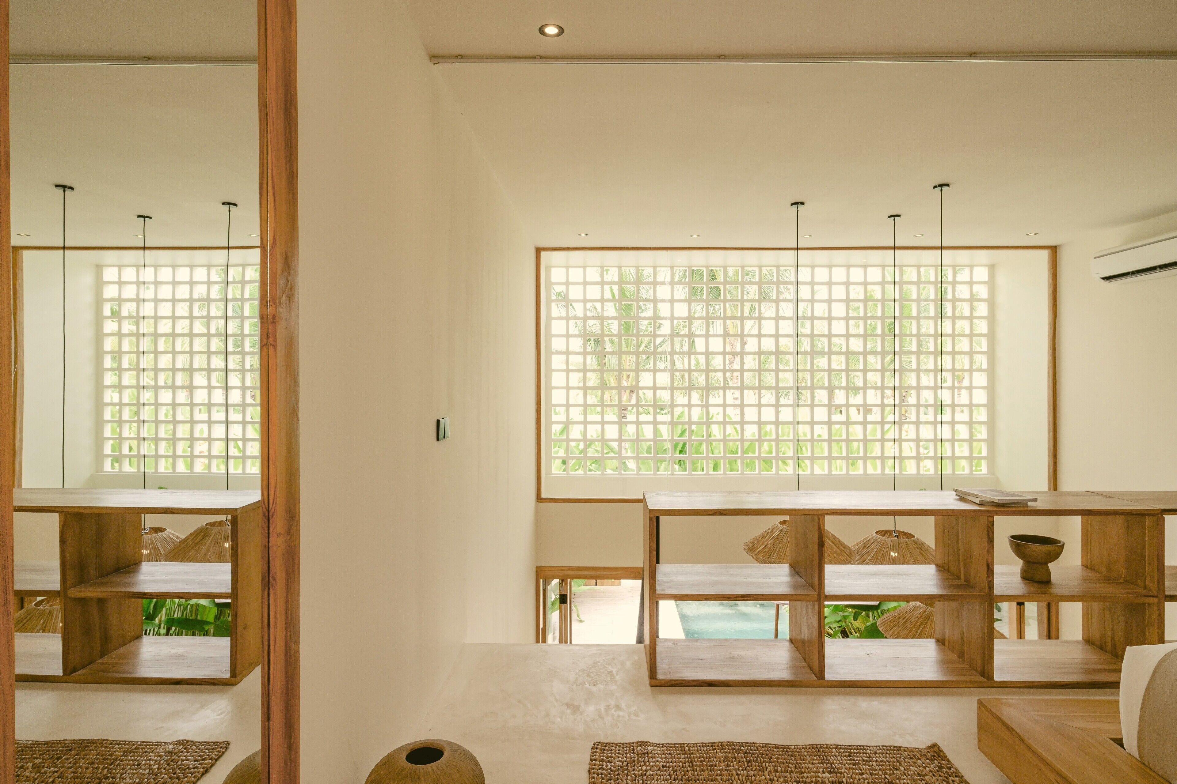 A room with a wooden floor, a large window with a grid pattern, and a wooden table with shelves.