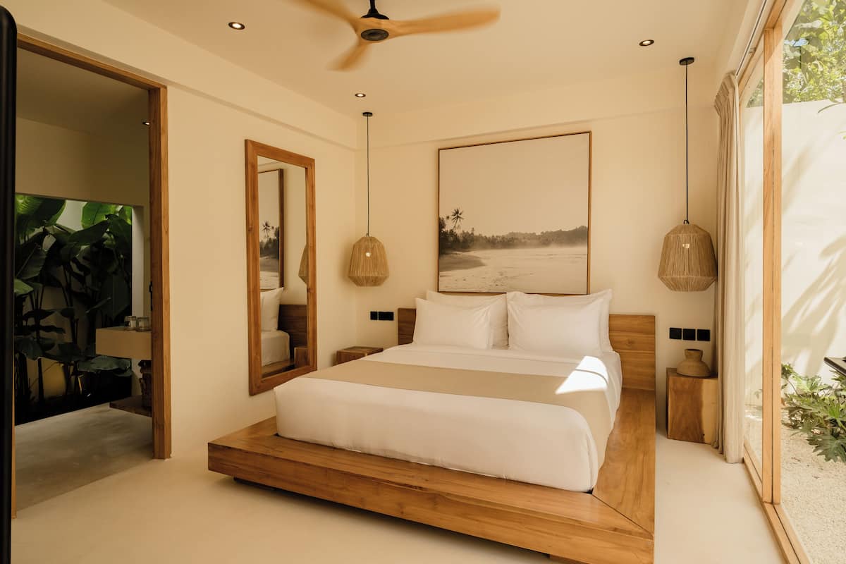 Ein modernes Schlafzimmer mit einem hölzernen Bett, einem Deckenventilator, einem großen Spiegel und einem Strand-Motiv-Gemälde.