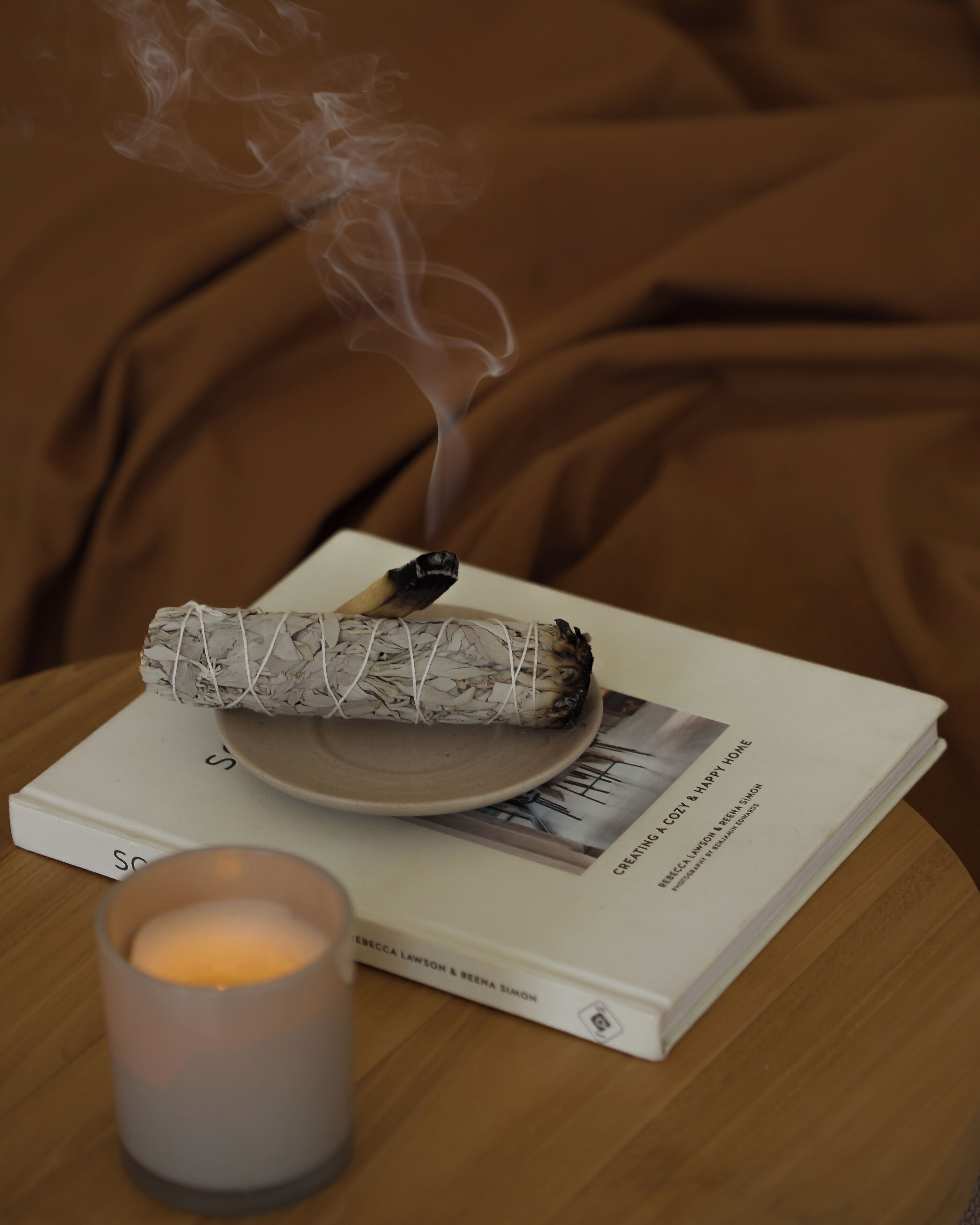 Un livre intitulé « Créer un intérieur chaleureux et agréable », avec un objet enroulé et une bougie allumée posés sur une surface en bois.