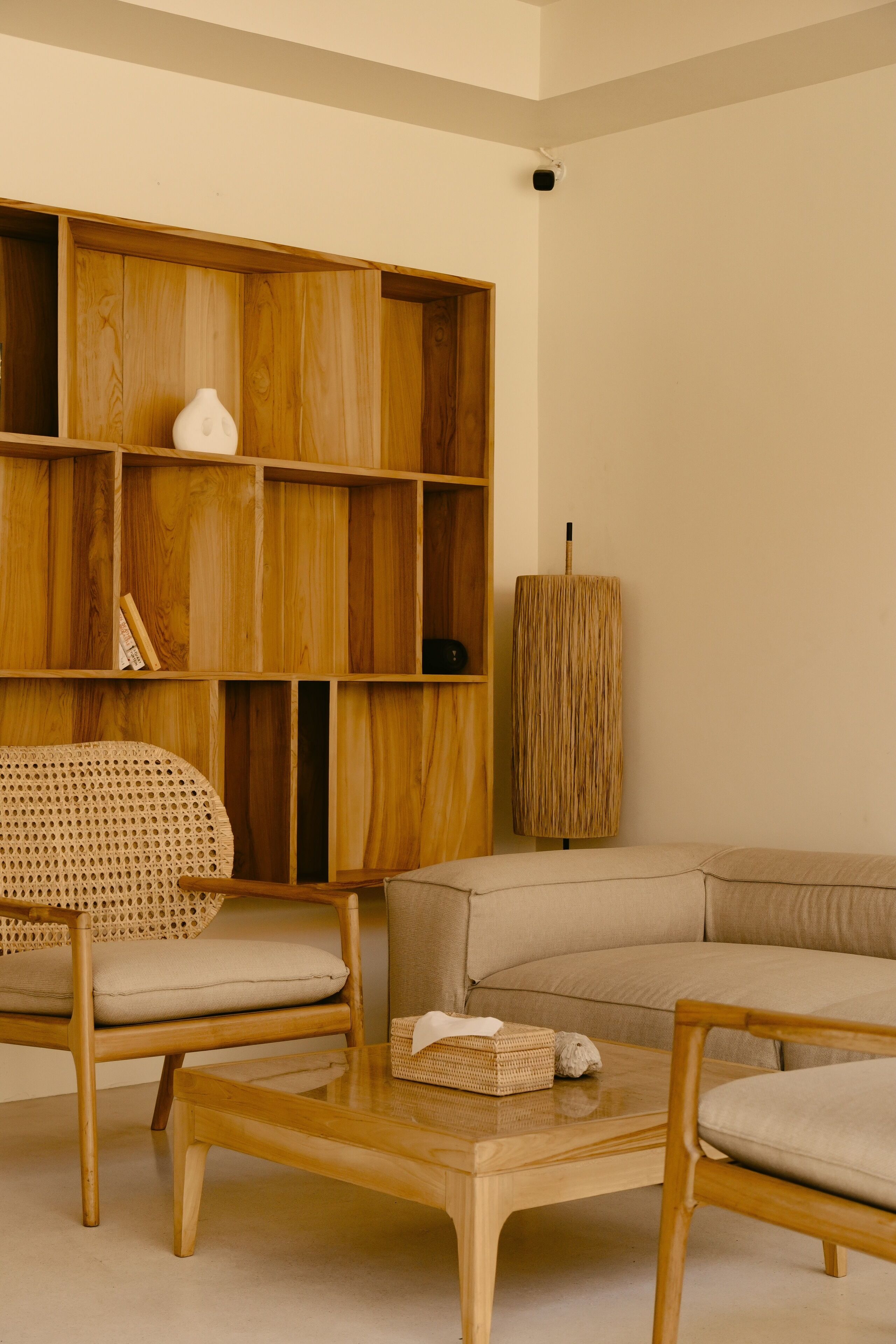A modern living room with a wooden bookshelf, a rattan chair, a beige sofa, and a coffee table.