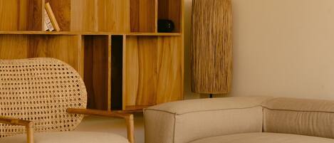 A modern living room with a wooden bookshelf, a rattan chair, a beige sofa, and a coffee table.