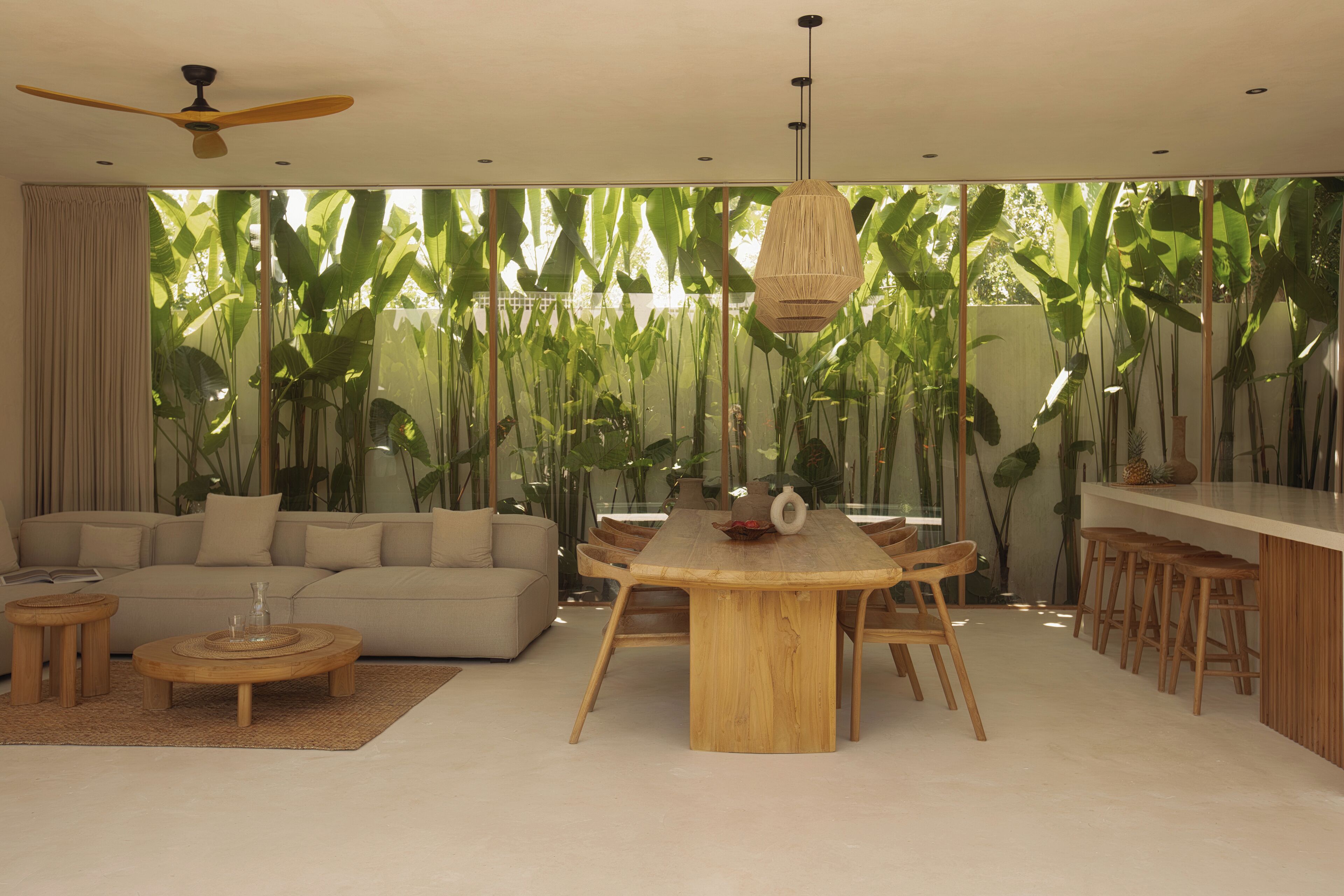 A modern living room with a round wooden dining table, beige sofa, and a ceiling fan.