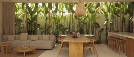 A modern living room with a round wooden dining table, beige sofa, and a ceiling fan.